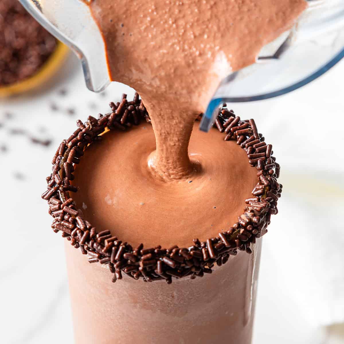 chocolate milkshake being poured from a blender container to a glass with a rim of chocolate sprinkles
