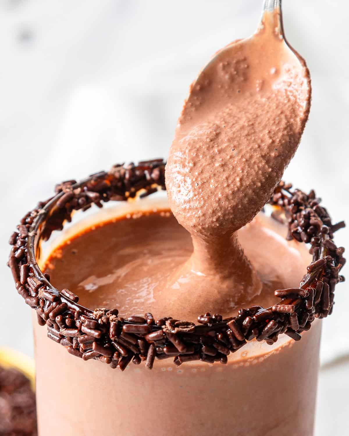 a spoon taking a scoop of chocolate milkshake in a glass