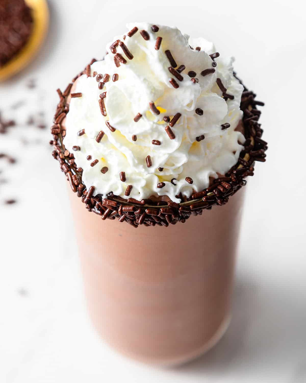 chocolate milkshake in a glass topped with whipped cream and chocolate sprinkles