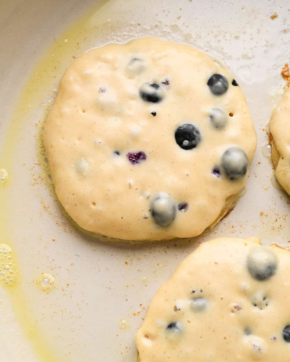 one blueberry pancake cooking on the first side in a pan
