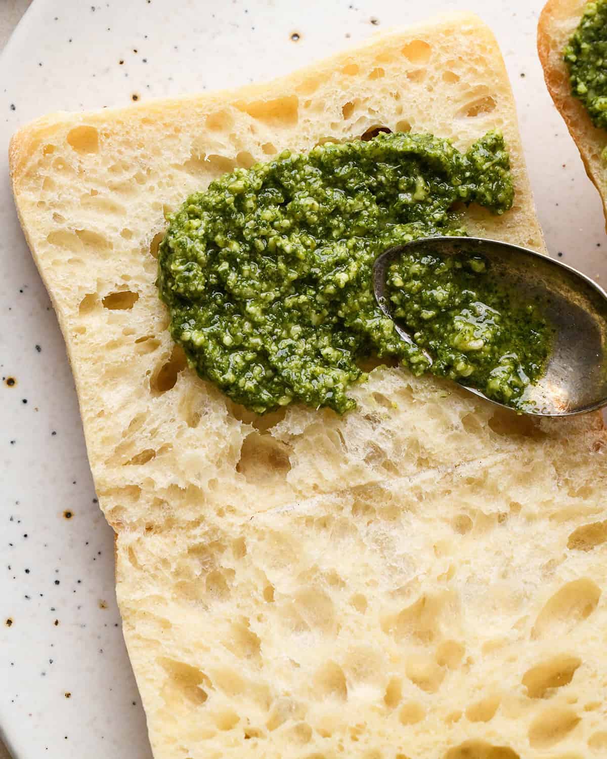 making a Caprese Sandwich - spreading pesto on a ciabatta roll