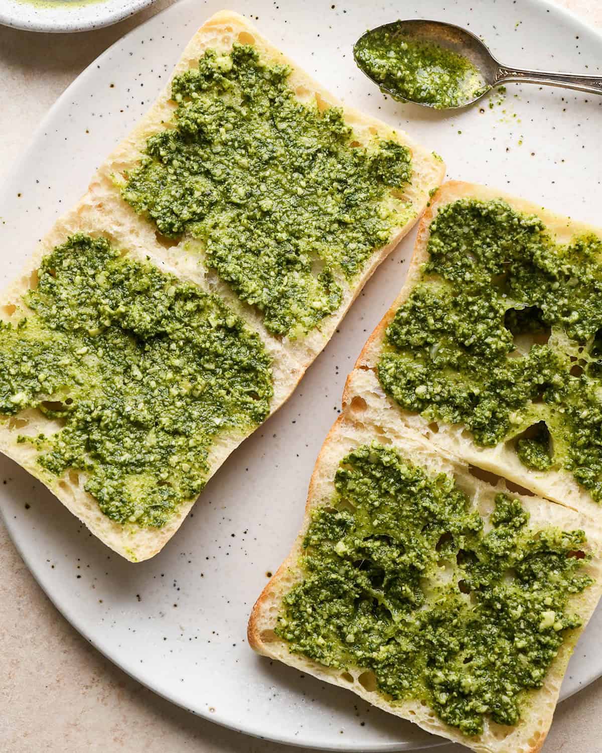 making Caprese Sandwiches - two ciabatta rolls on a plate spread with pesto