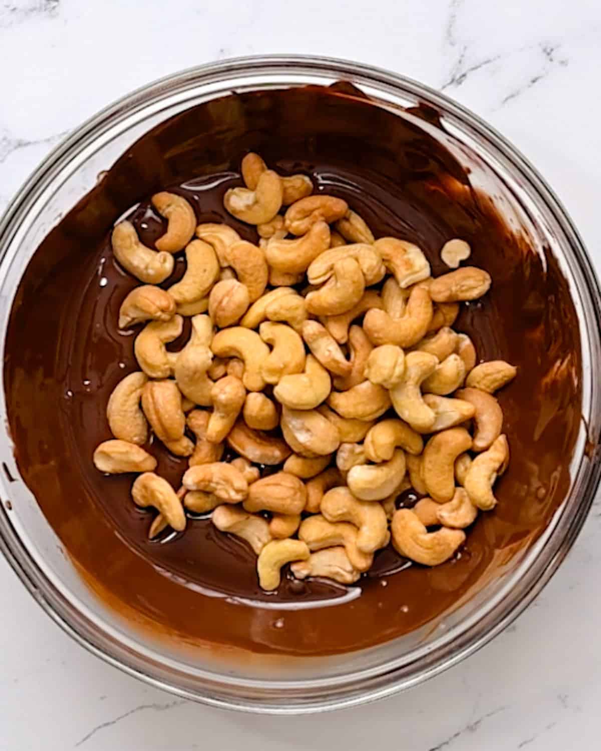 How to Make Chocolate Covered Cashews - cashews added to melted chocolate in a bowl before stirring