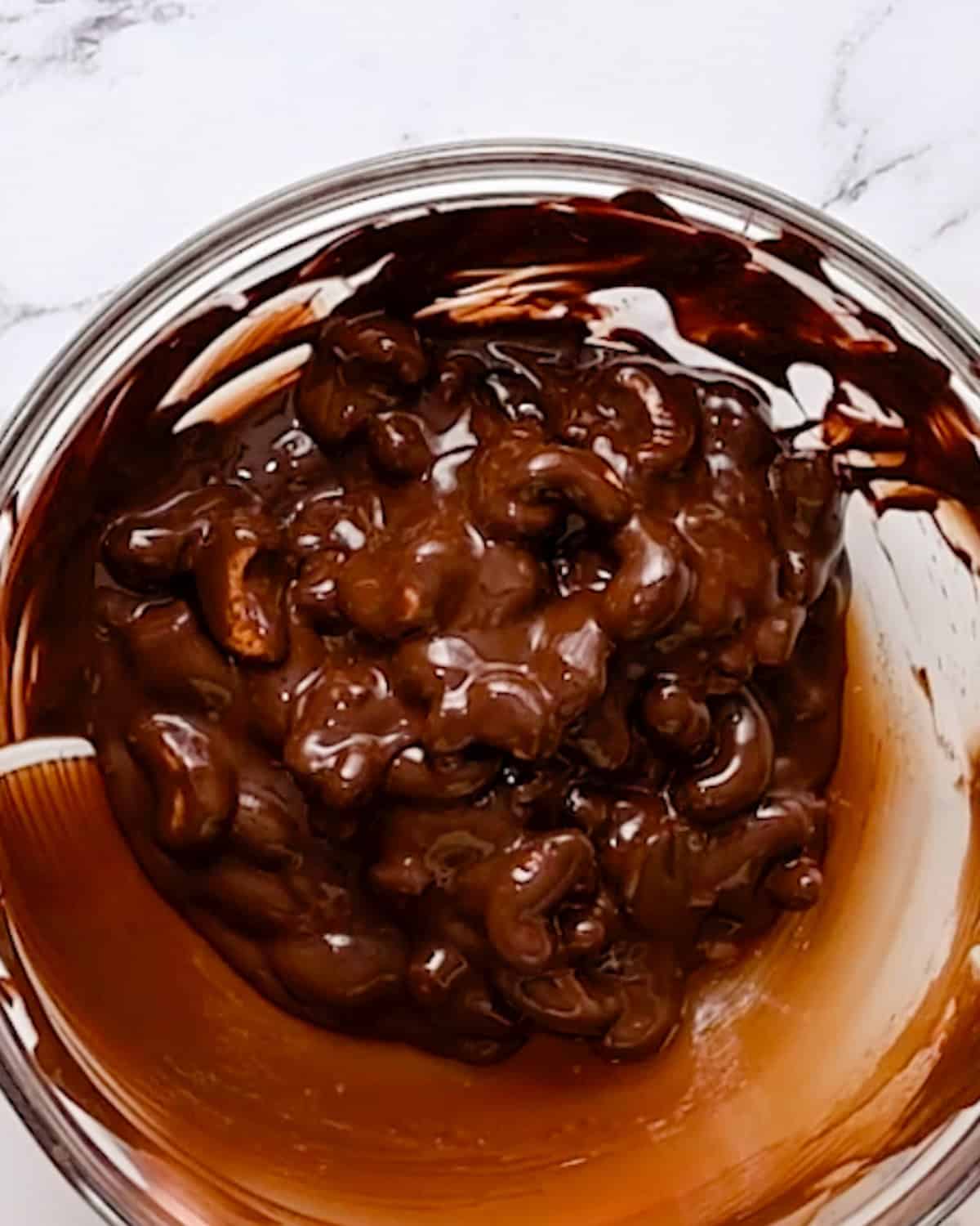 How to Make Chocolate Covered Cashews - cashews coated in melted chocolate in a bowl. 