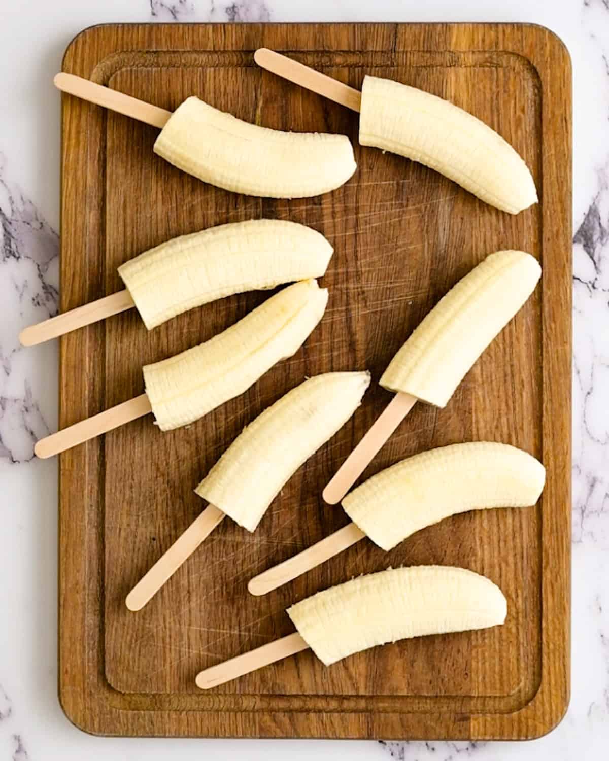 banana halves with popsicle sticks in them on a cutting board