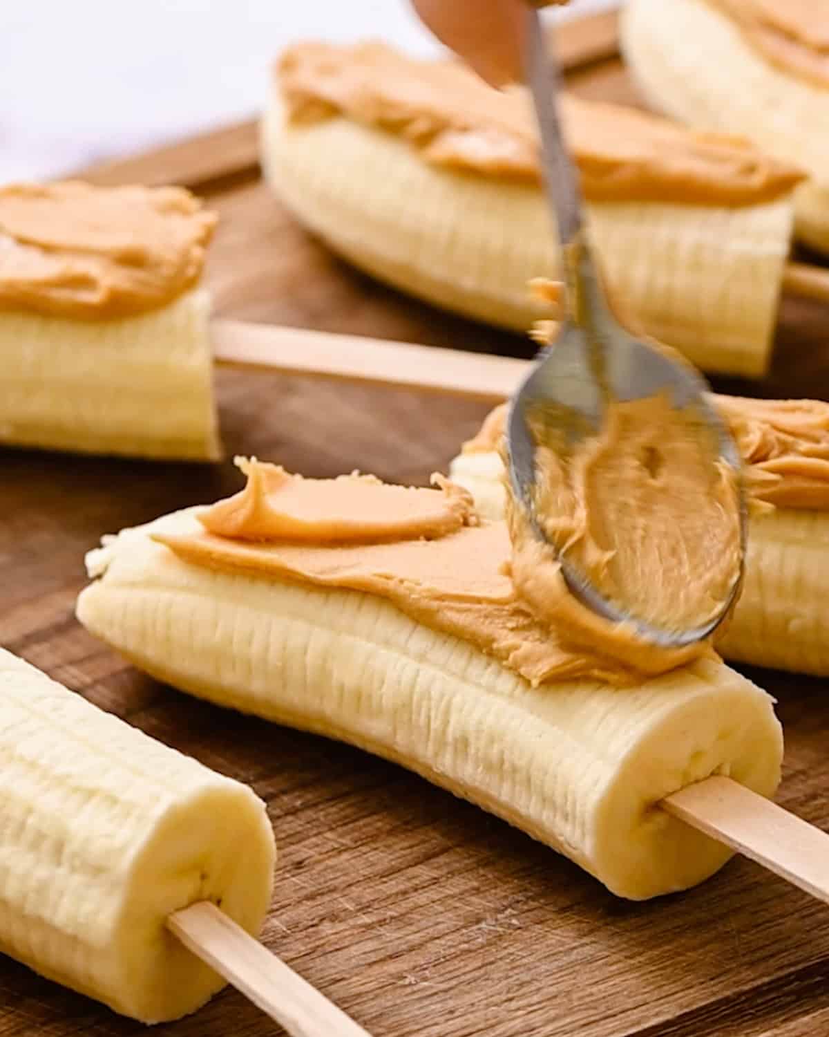 a spoon spreading peanut butter on a half of a banana to make Chocolate Peanut Butter Frozen Bananas