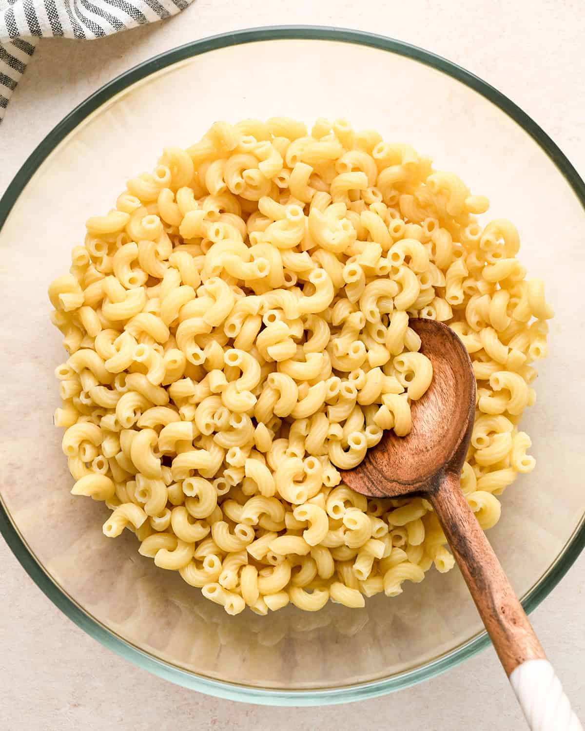 How to Make Macaroni Salad - cooked macaroni in a bowl with a wooden spoon