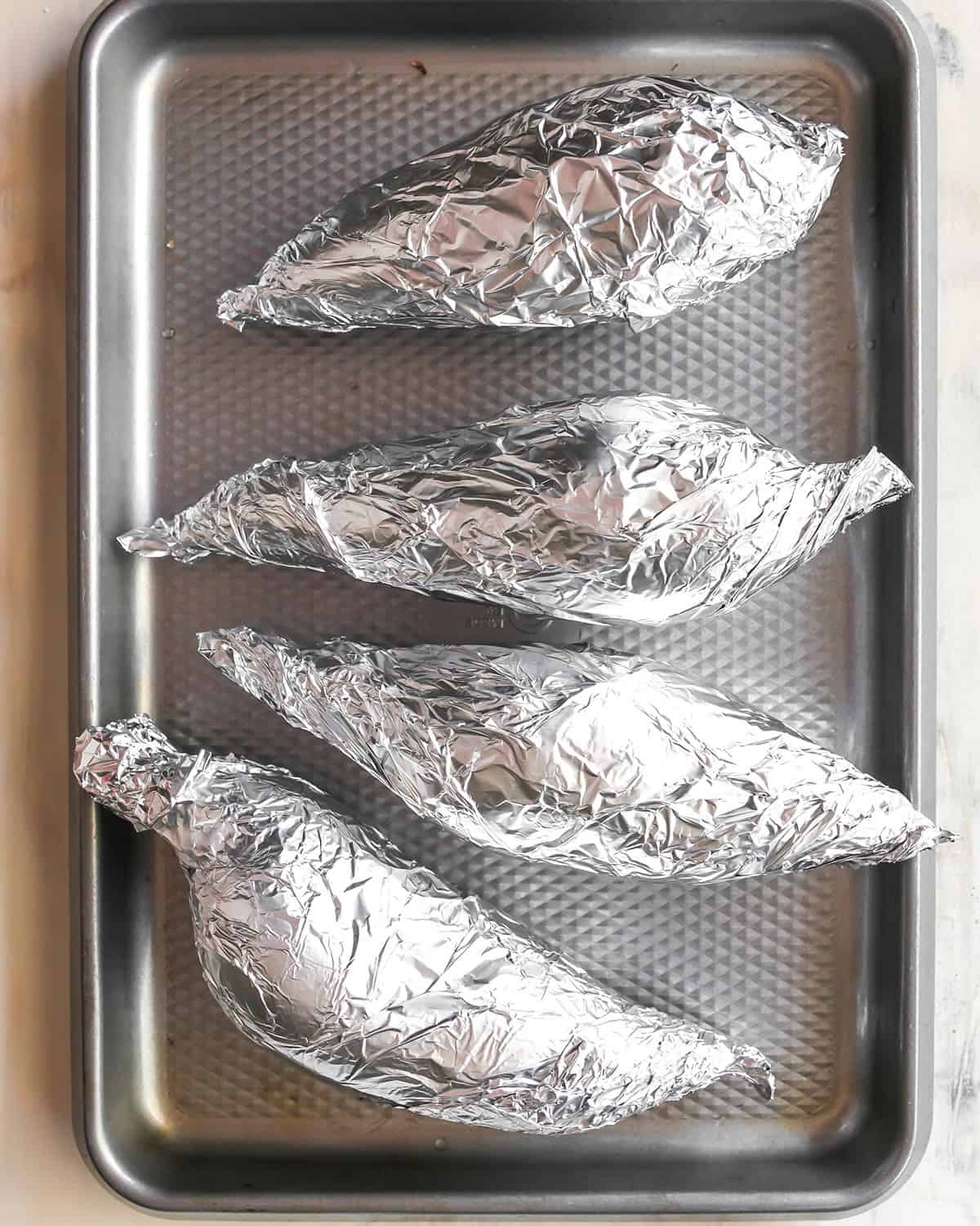How to Make Sweet Potato Baby Food - sweet potatoes wrapped in foil on a baking sheet