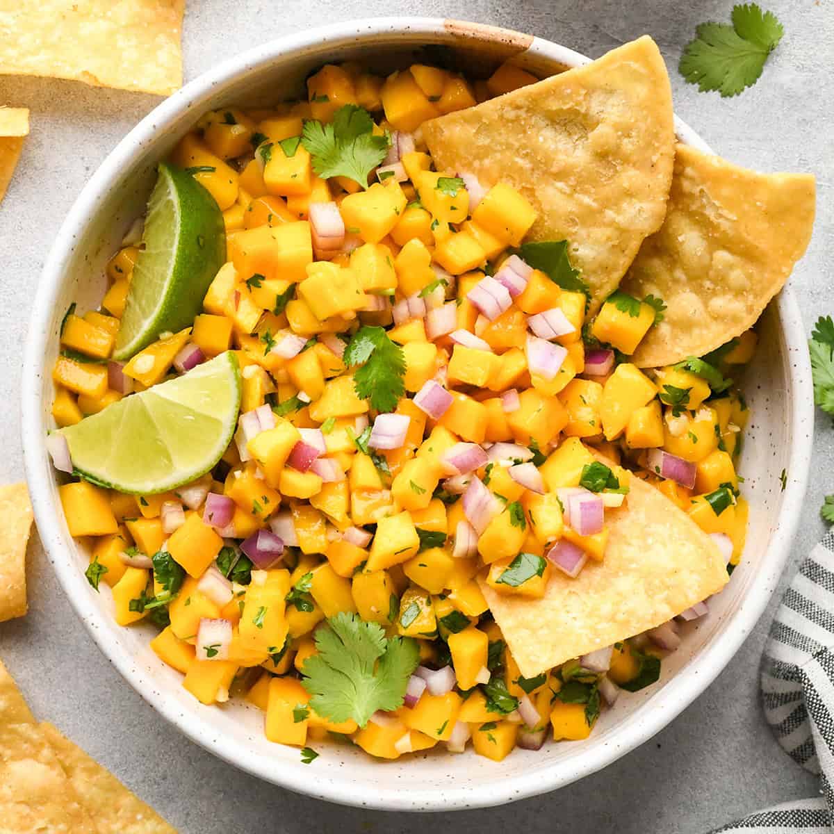Mango Salsa in a bowl with chips, lime and cilantro