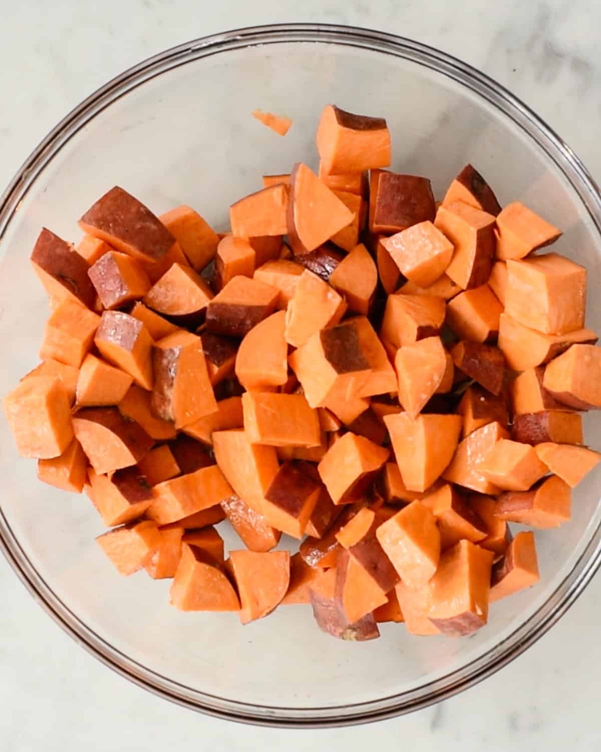 how to make Cinnamon Roasted Sweet Potatoes - sweet potato cubes in a bowl coated in melted butter