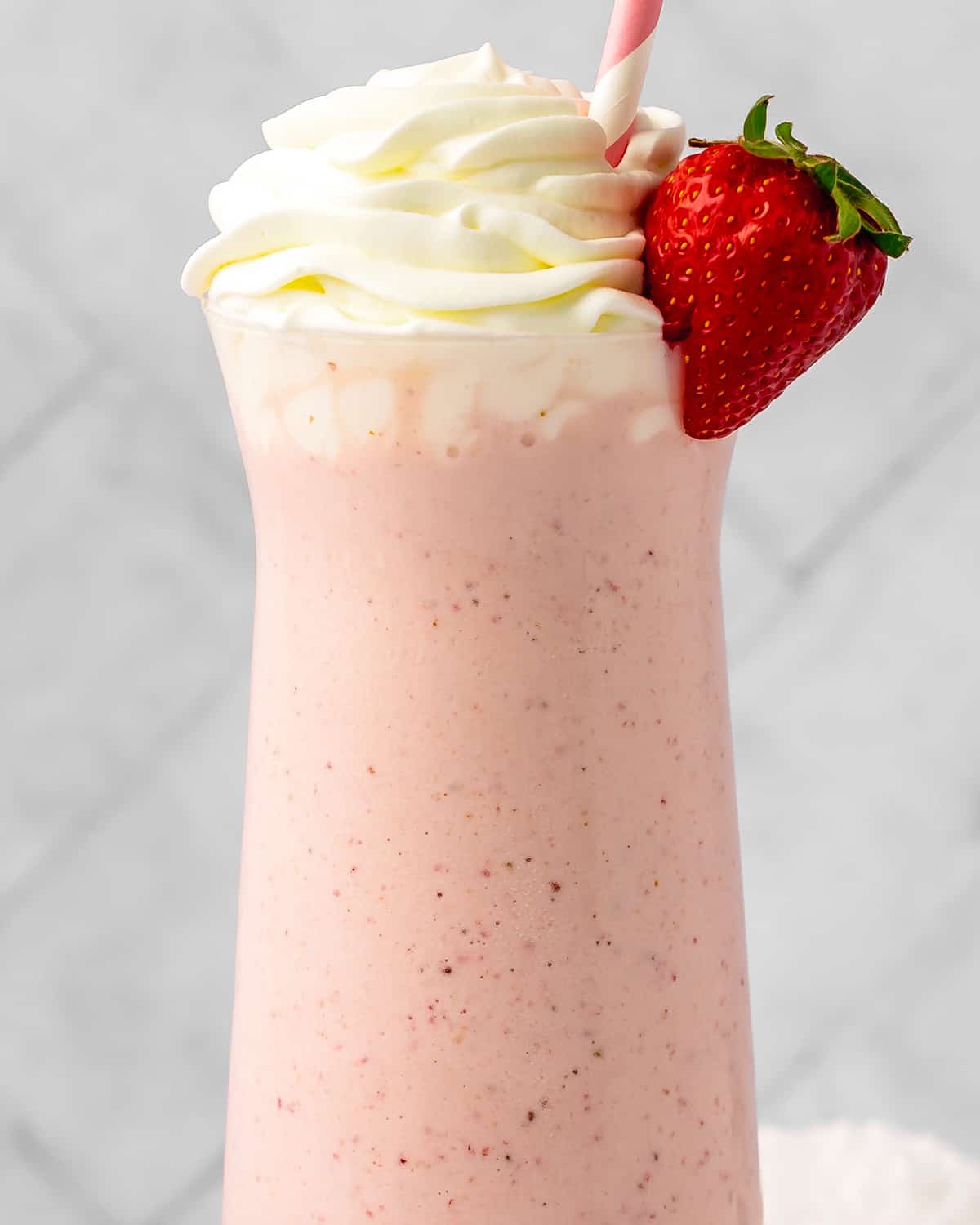 up close photo of Strawberry Milkshake in a glass with whipped cream and a strawberry