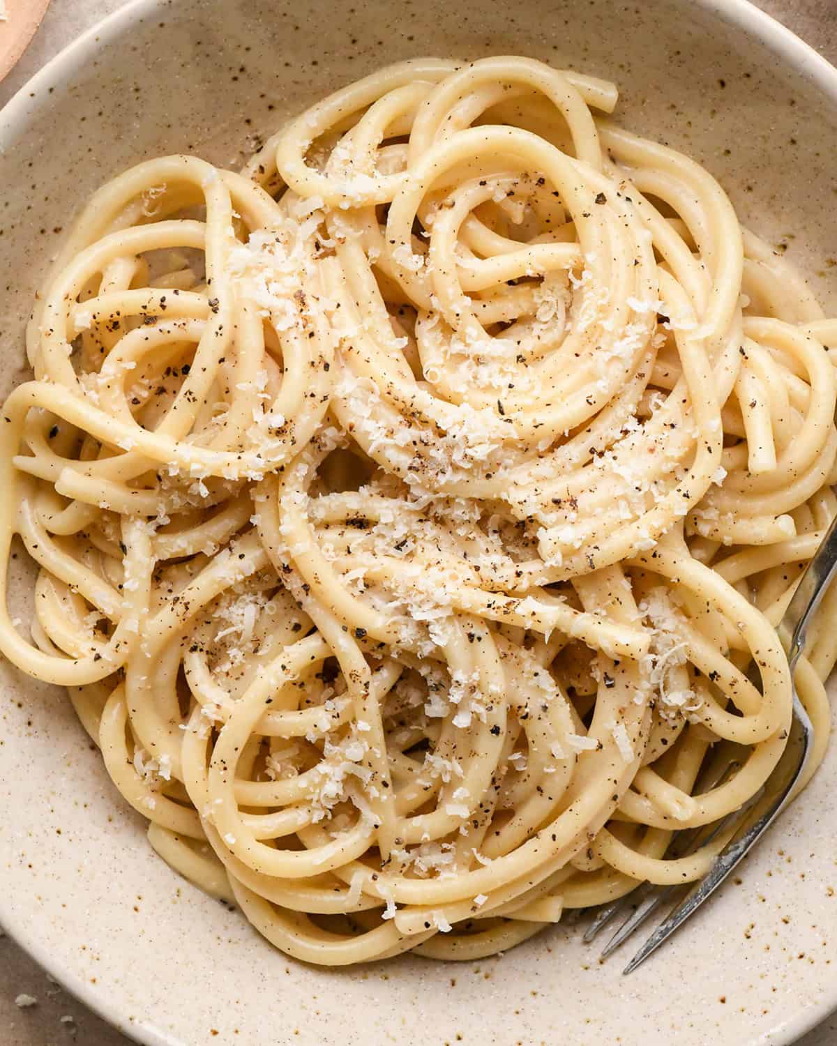 Cacio e Pepe Pasta in a bowl with a fork topped with parmesan cheese and pepper