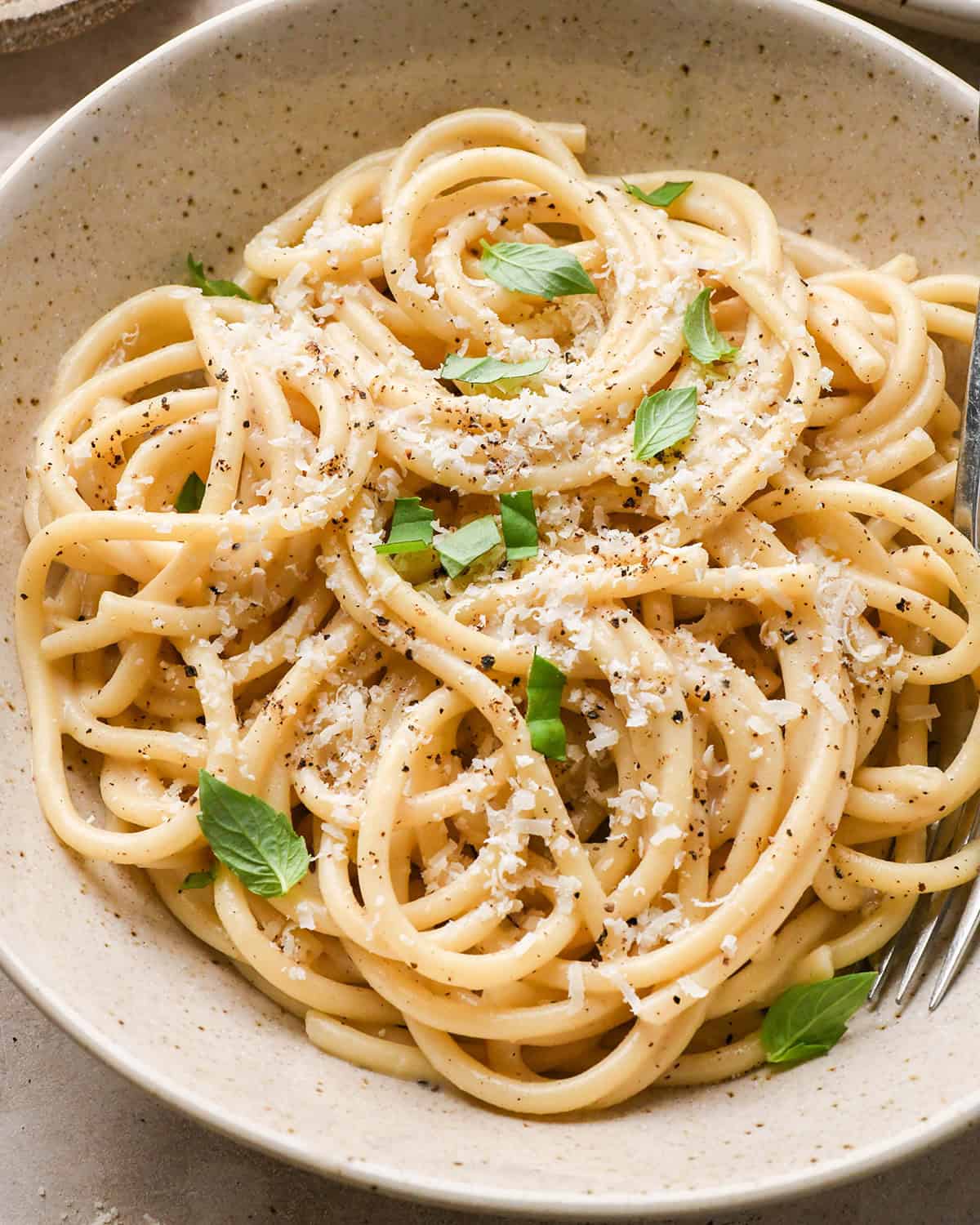 Cacio e Pepe Pasta in a bowl garnished with parmesan, pepper and fresh basil