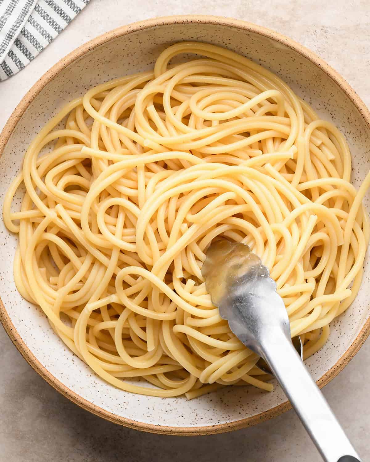 bucatini pasta being put into a bowl with tongs to make Cacio e Pepe Pasta