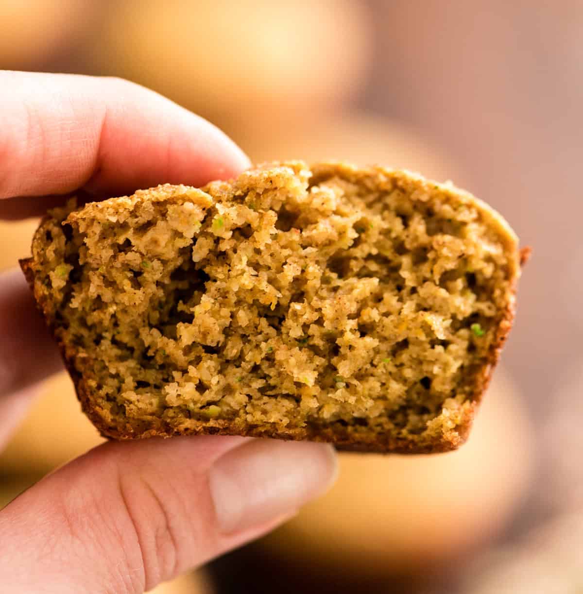 a hand holding a half of a Carrot Zucchini Muffin so the texture is visible