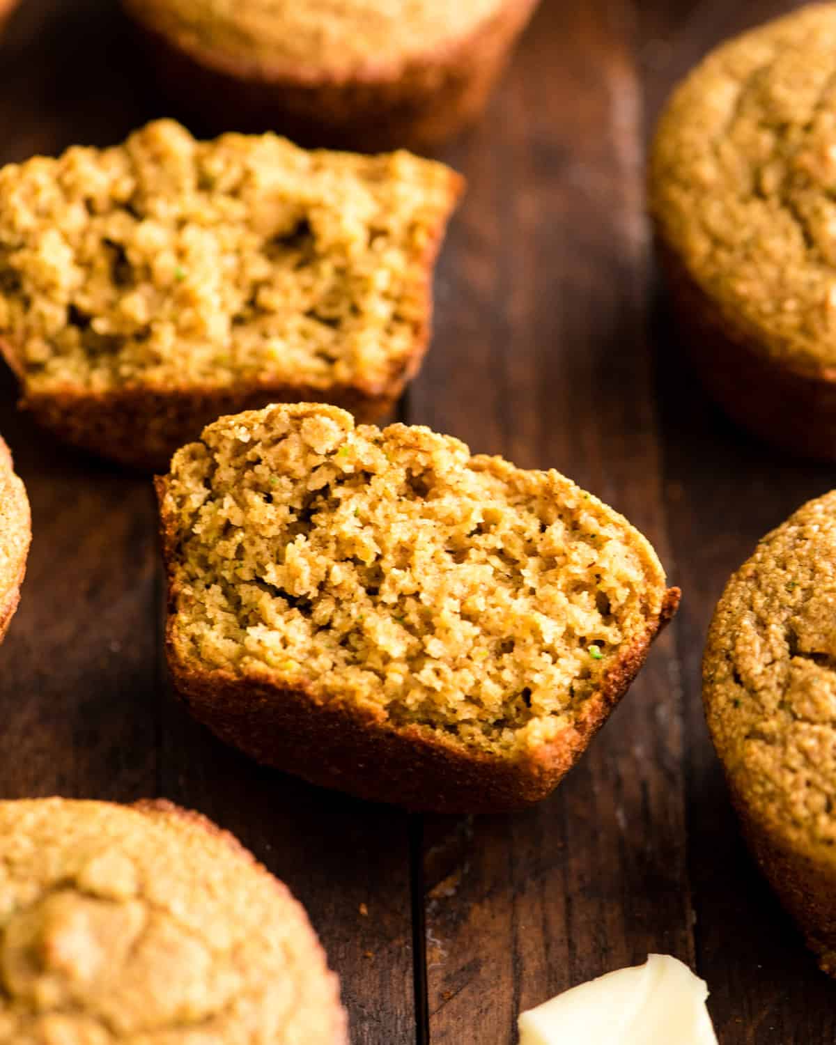a Carrot Zucchini Muffin cut in half so the texture is visible surrounded by other whole muffins