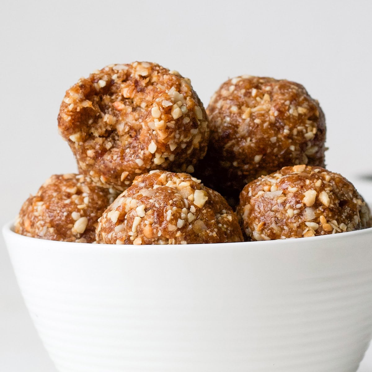 5 Cashew Coconut Date Balls in a bowl, one with a bite taken out of it