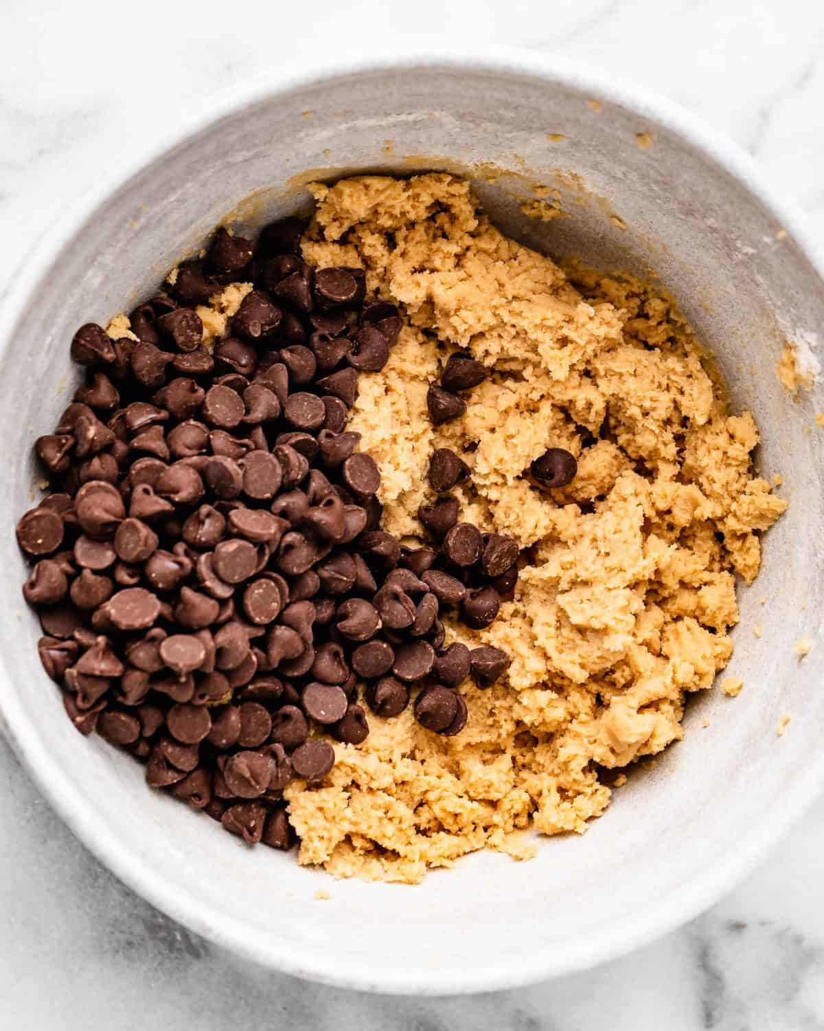making cherry cookies - chocolate chips added to the dough n a white ceramic mixing bowl on a marble surface before mixing