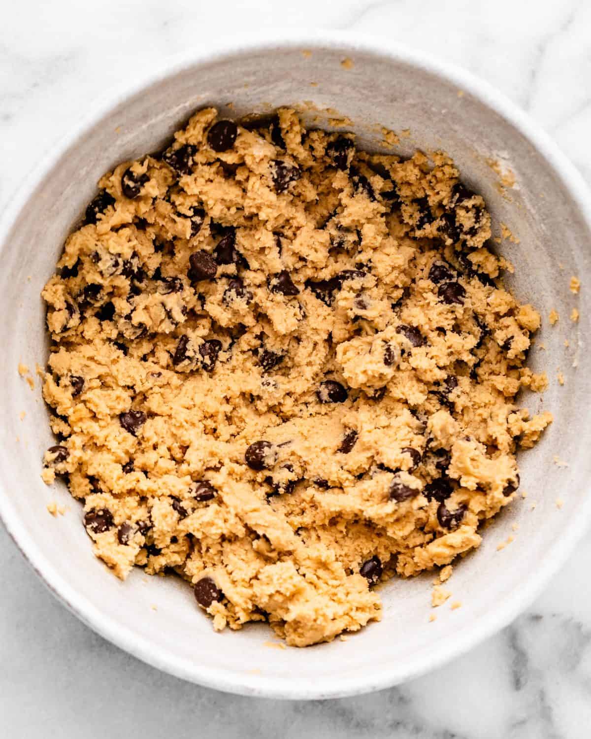 making cherry cookies - chocolate chips mixed into the dough in a white ceramic mixing bowl on a marble surface