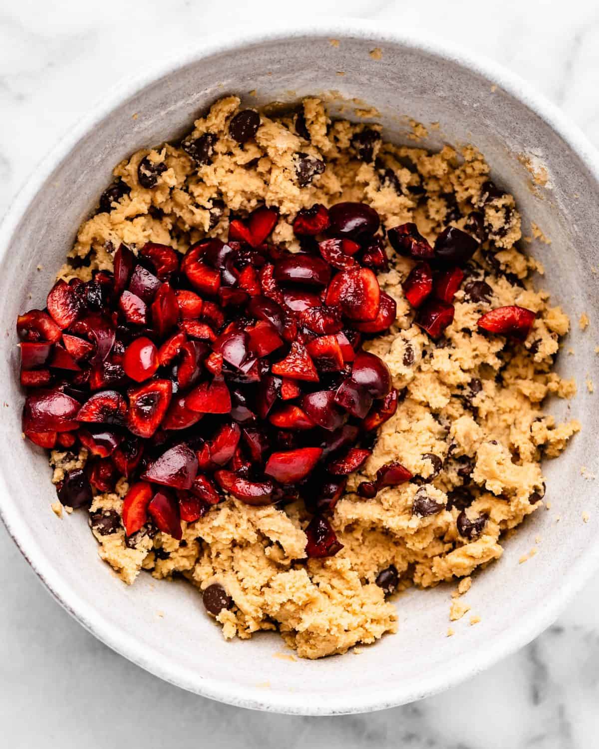making cherry cookies - cherries added to the dough in a white ceramic mixing bowl on a marble surface before mixing