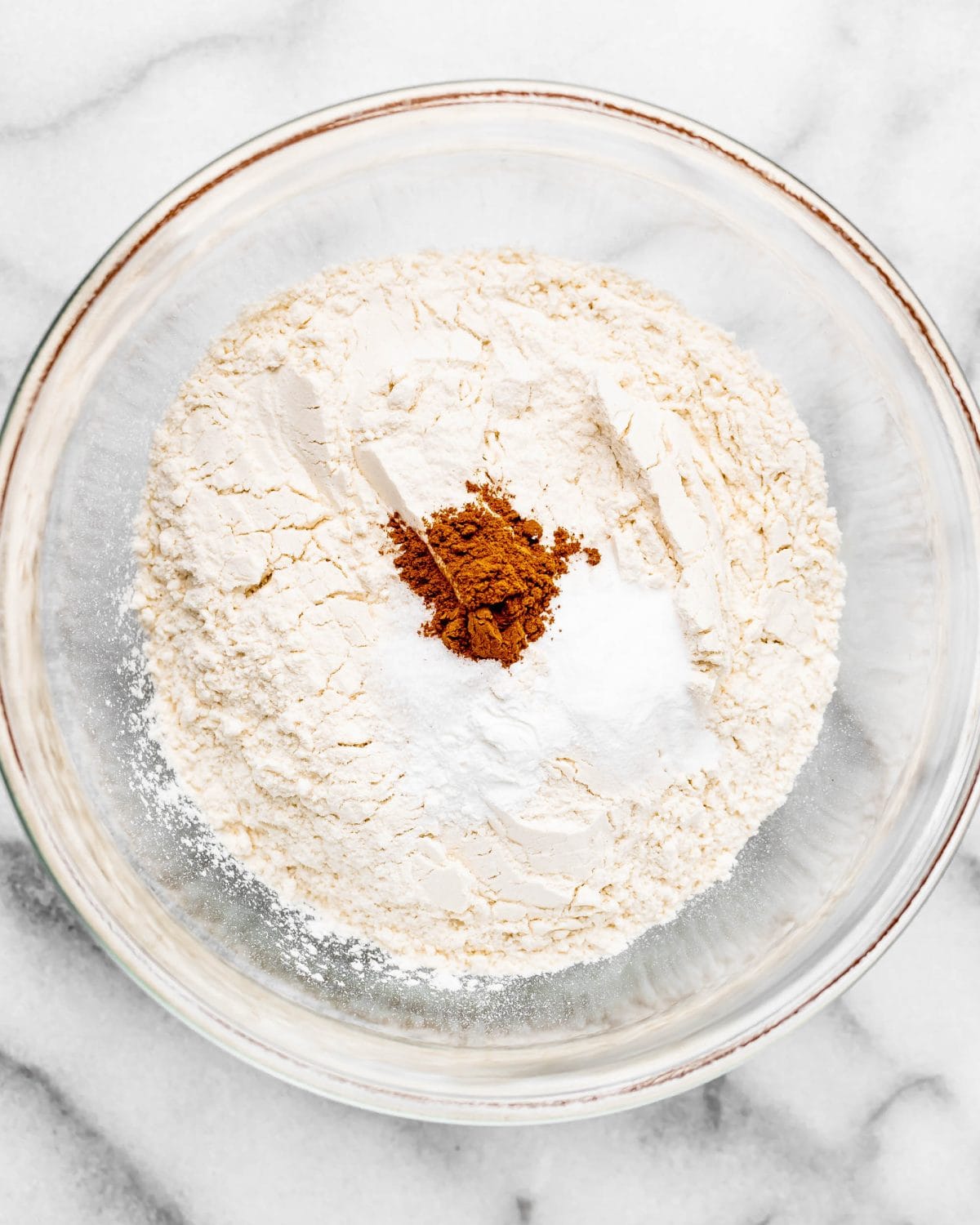 making cherry cookies - flour, baking soda, baking powder, salt and cinnamon in a glass mixing bowl on a marble surface before mixing