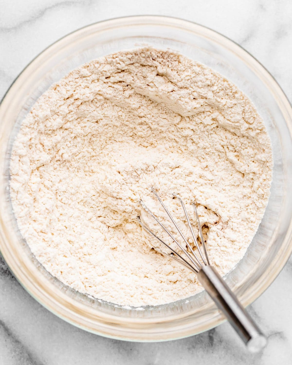 making cherry cookies - flour, baking soda, baking powder, salt and cinnamon in a glass mixing bowl on a marble surface after mixing with a wire whisk that is also in the bowl