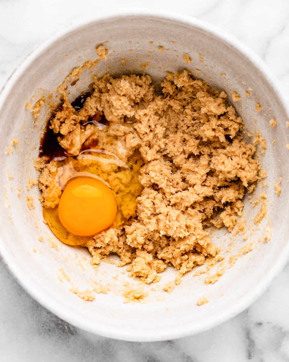 making cherry cookies - vanilla and egg added to the beaten butter mixture in a white ceramic mixing bowl on a marble surface before mixing