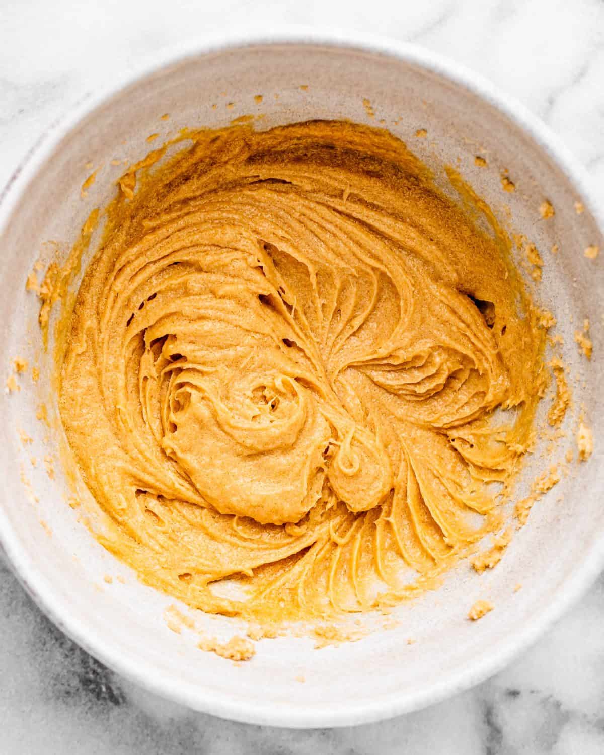 making cherry cookies - beaten wet ingredient mixture in a white ceramic mixing bowl on a marble surface after being beaten together