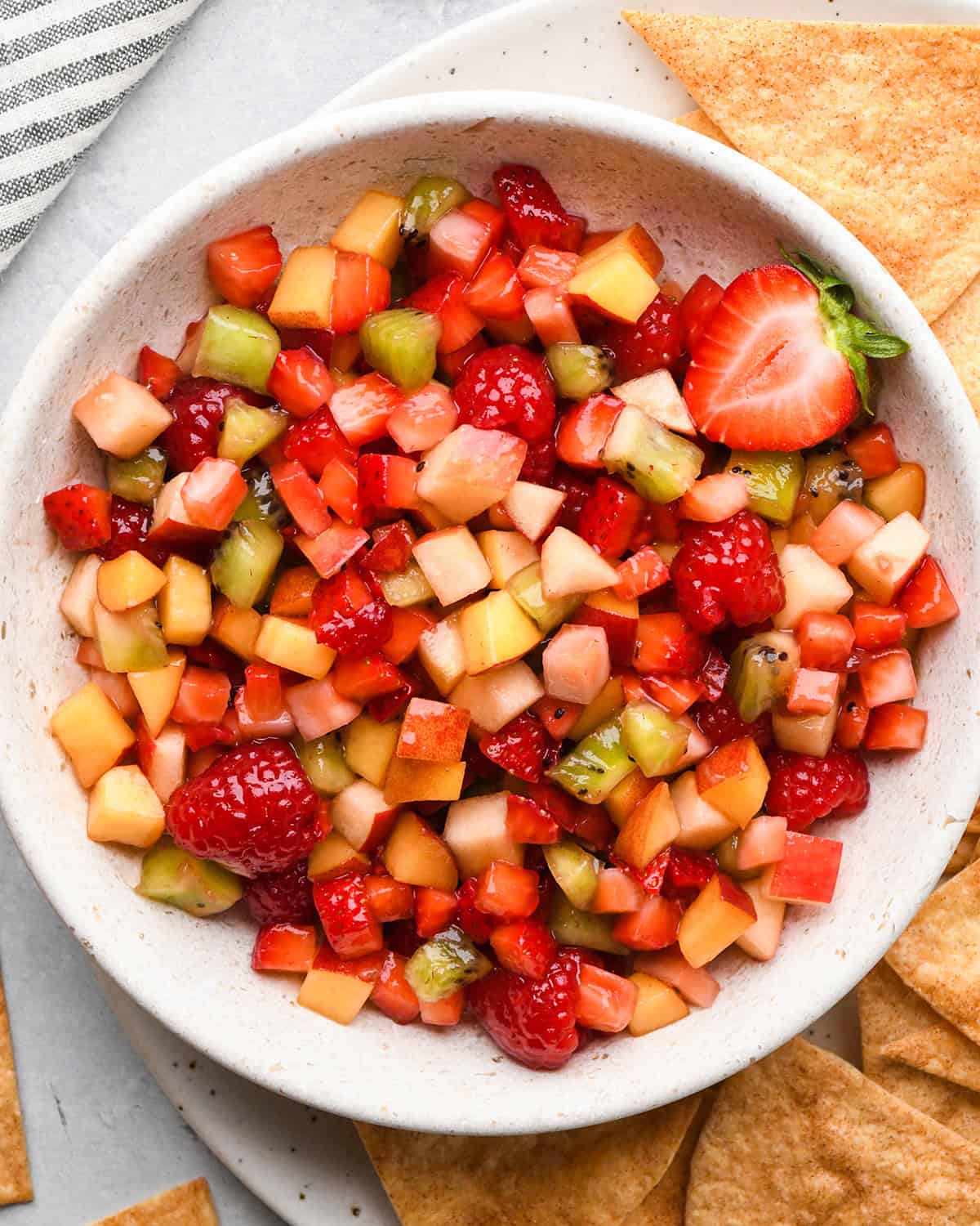 overhead photo of a bowl of fruit salsa with cinnamon chips around it