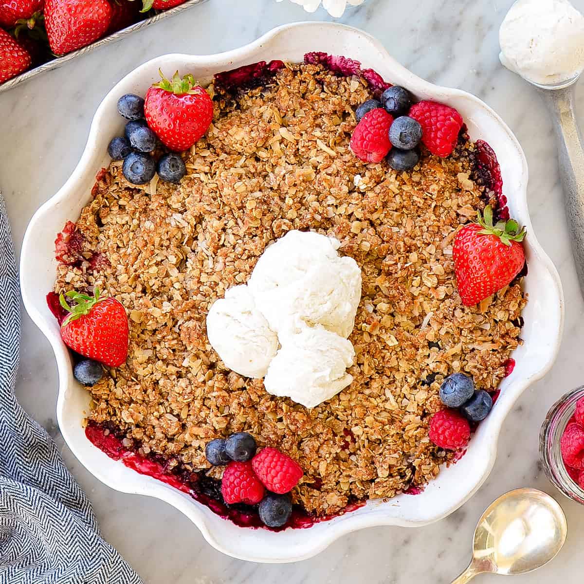 healthy berry crisp in a pie dish after baking with ice cream and more berries