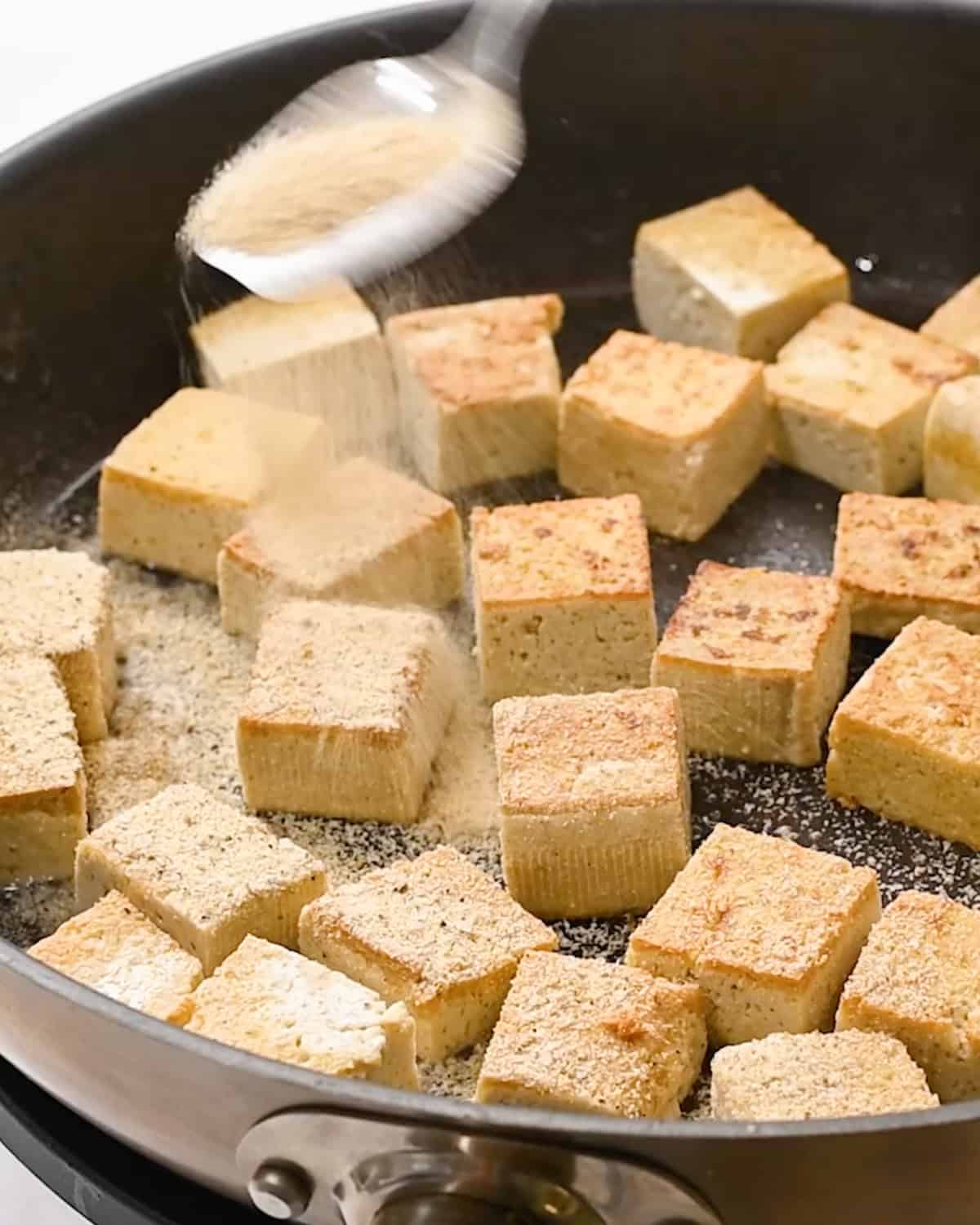 spice mixture being sprinkled over tofu in a pan