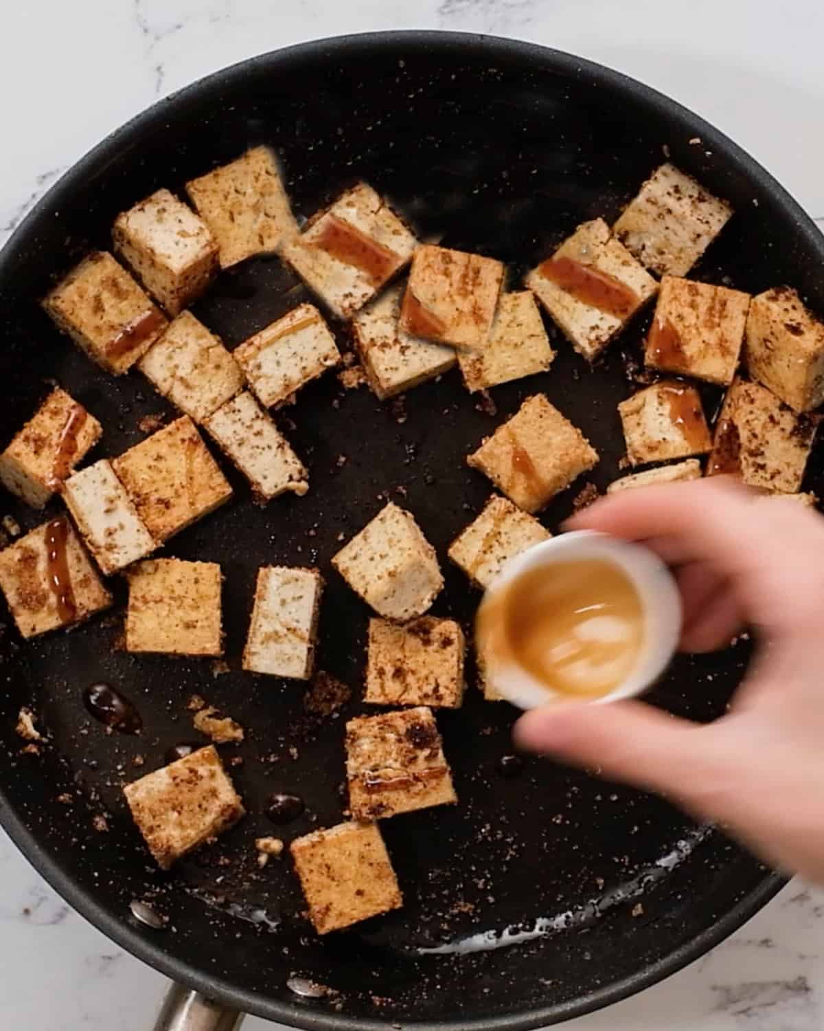hoisin sauce being drizzled over tofu in a pan
