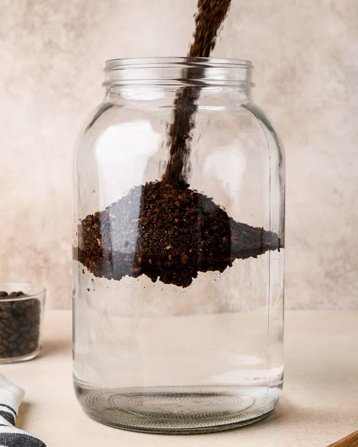 How to Make Cold Brew Coffee Recipe - coffee grounds being poured into the glass jar with water