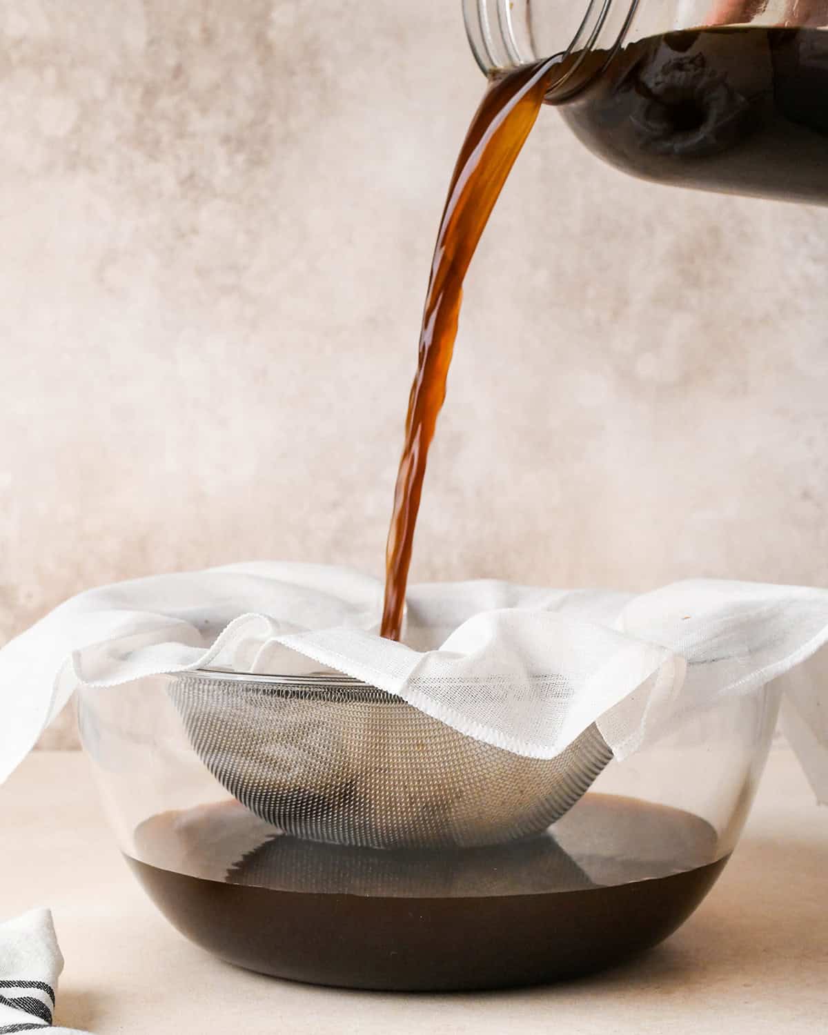How to Make Cold Brew Coffee Recipe - straining coffee grounds through a cheesecloth and fine mesh strainer