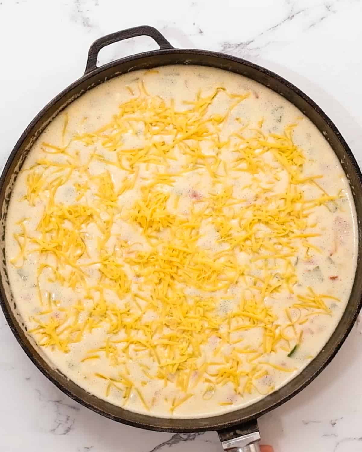 gluten free crustless quiche in a skillet before baking with cheese on top 