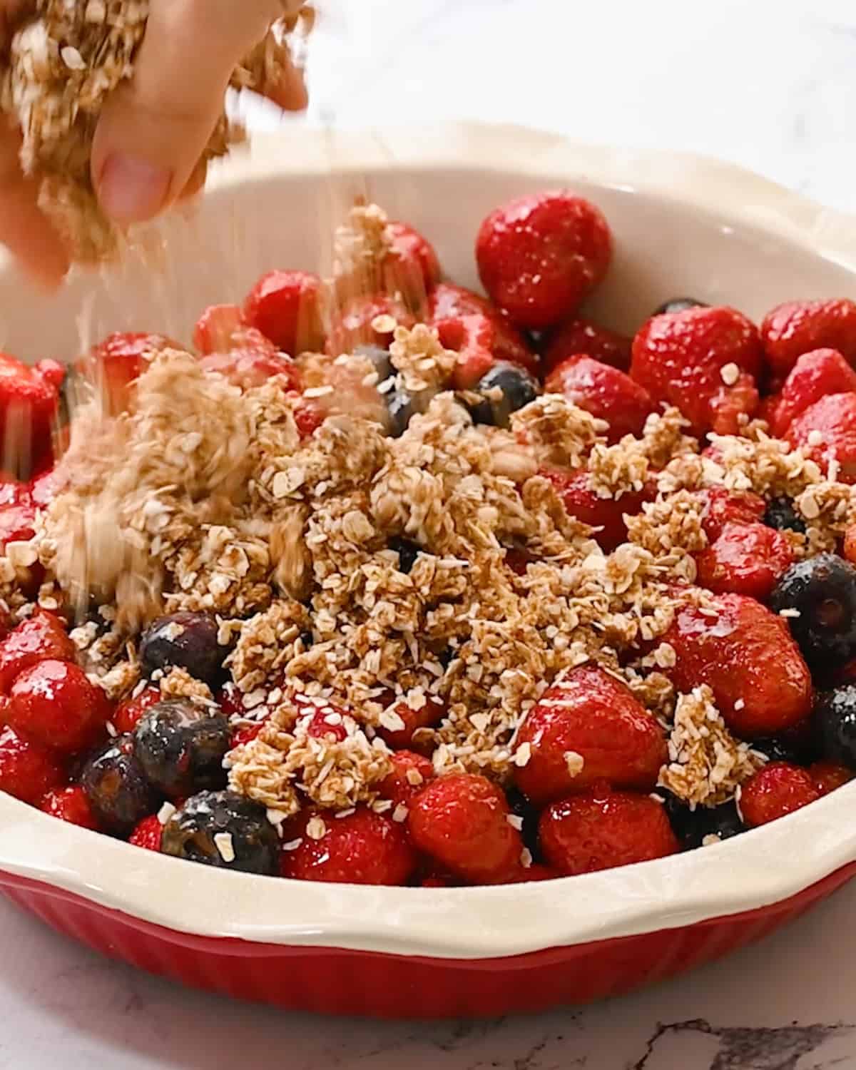 How to Make Healthy Berry Crisp -  topping being sprinkled on the berries in the pie dish