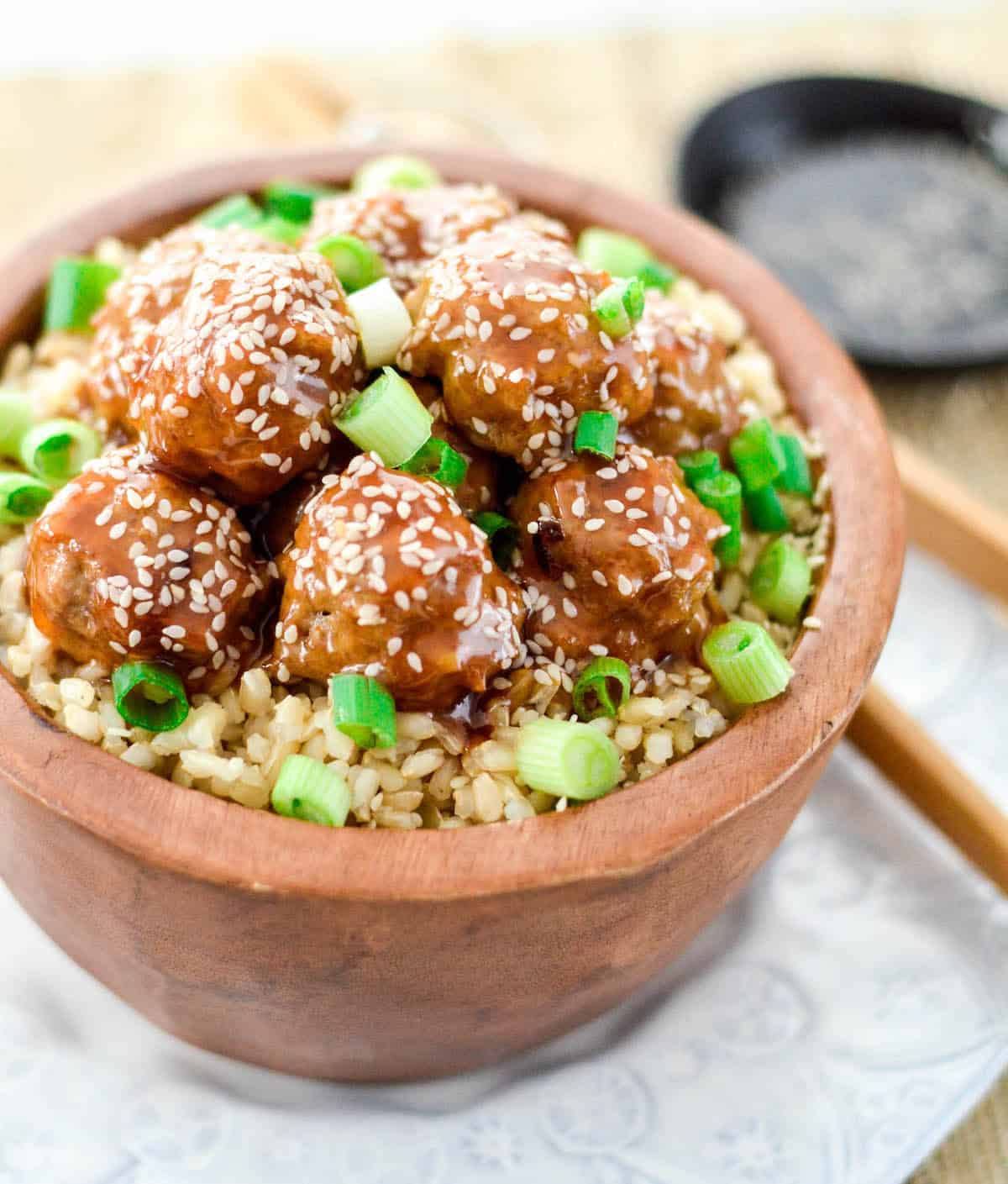 Paleo Sweet and Sour Meatballs in a bowl with brown rice, green onions and sesame seeds