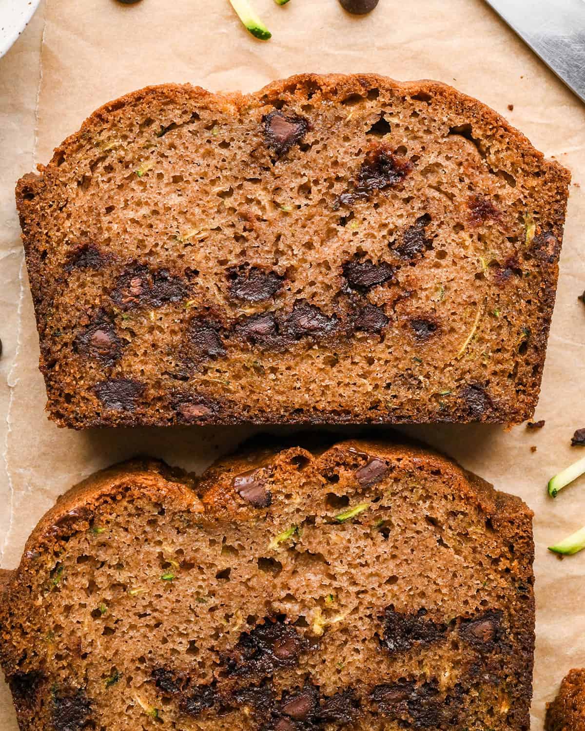 close up of two slices of chocolate chip zucchini bread and the loaf on parchment paper 