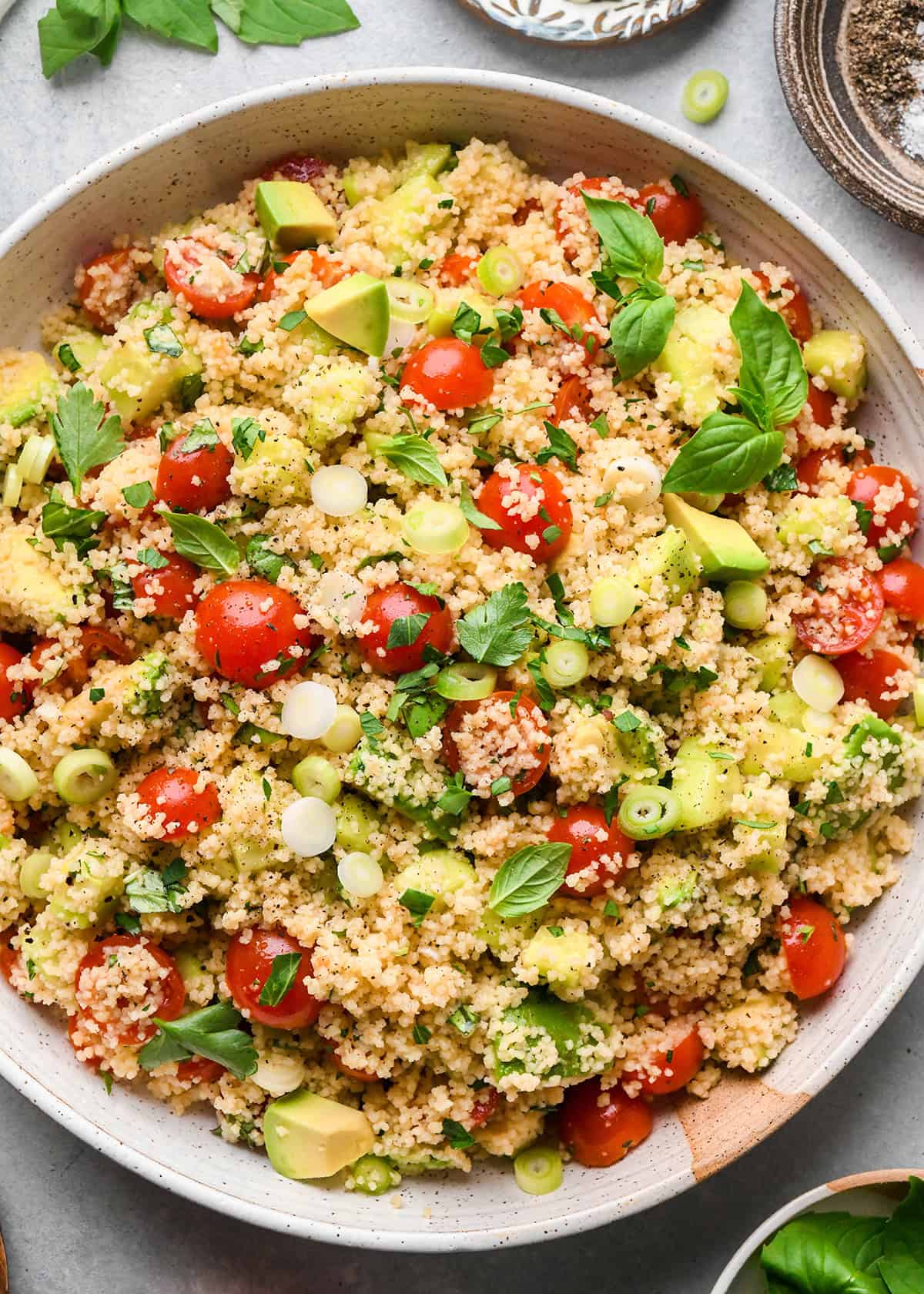 couscous salad with cherry tomatoes, avocado, green onions, and fresh herbs in a serving bowl