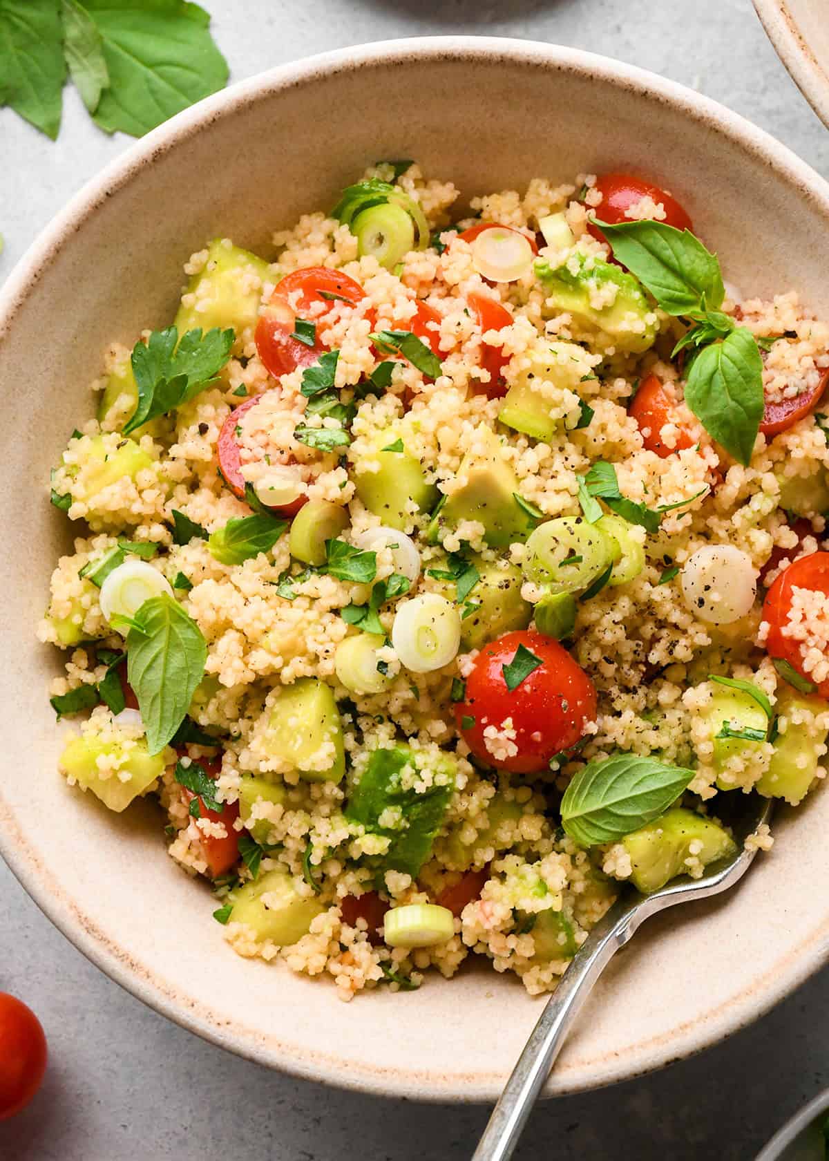 couscous salad with cherry tomatoes, avocado, green onions, and fresh herbs in a small bowl with a fork
