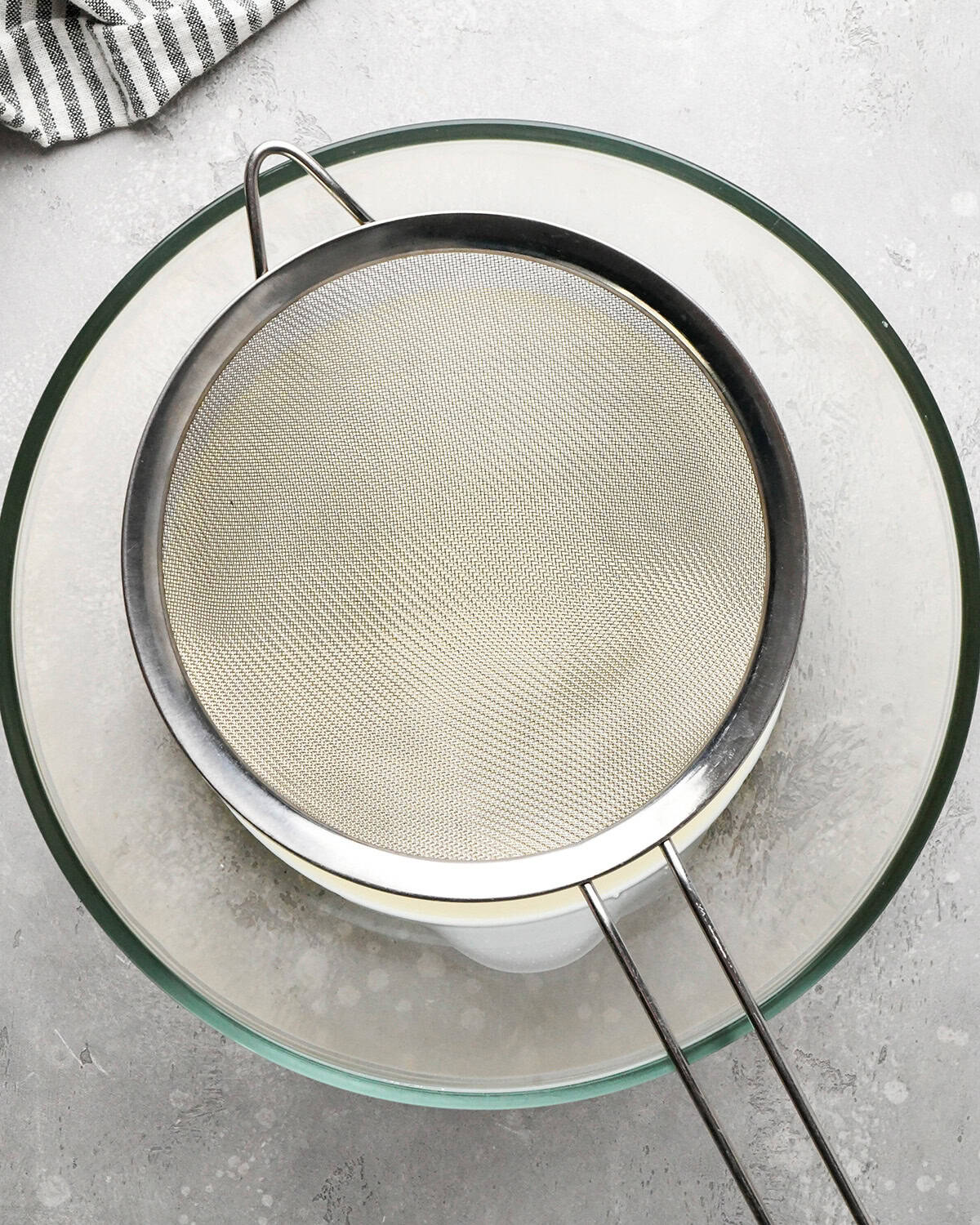 a metal strainer over heavy cream in a glass bowl
