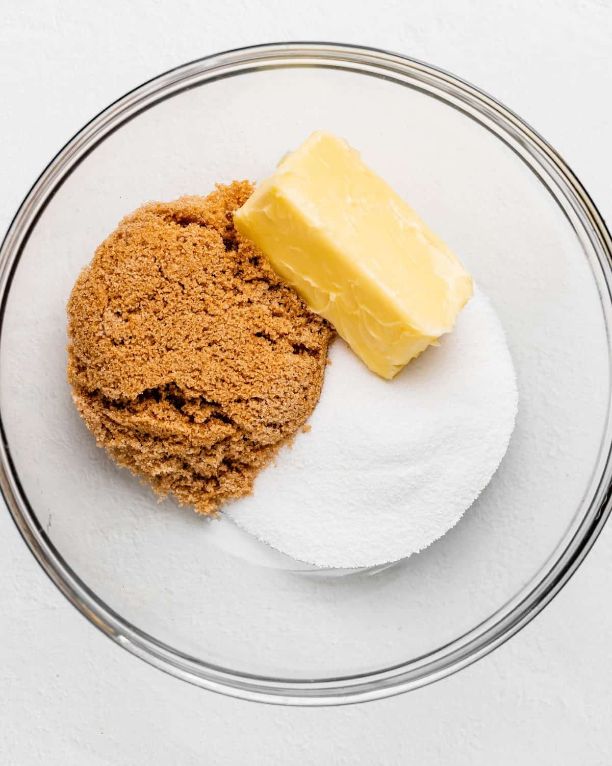 making s'mores cookies recipe - a stick of softened butter, white sugar and brown sugar in a glass mixing bowl before mixing