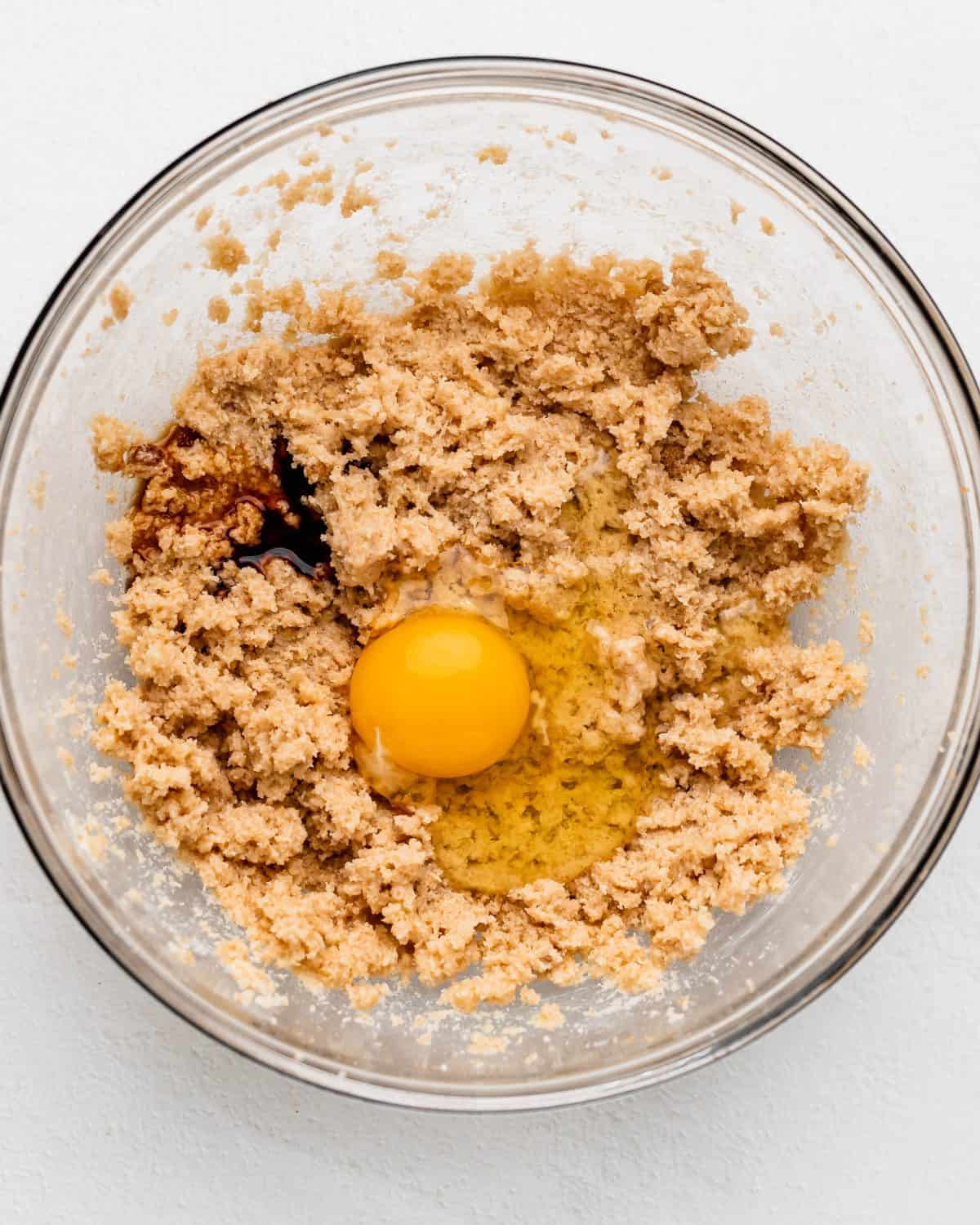making s'mores cookies recipe - vanilla and egg added to the beaten butter and sugar mixture before mixing in a glass bowl on a white surface