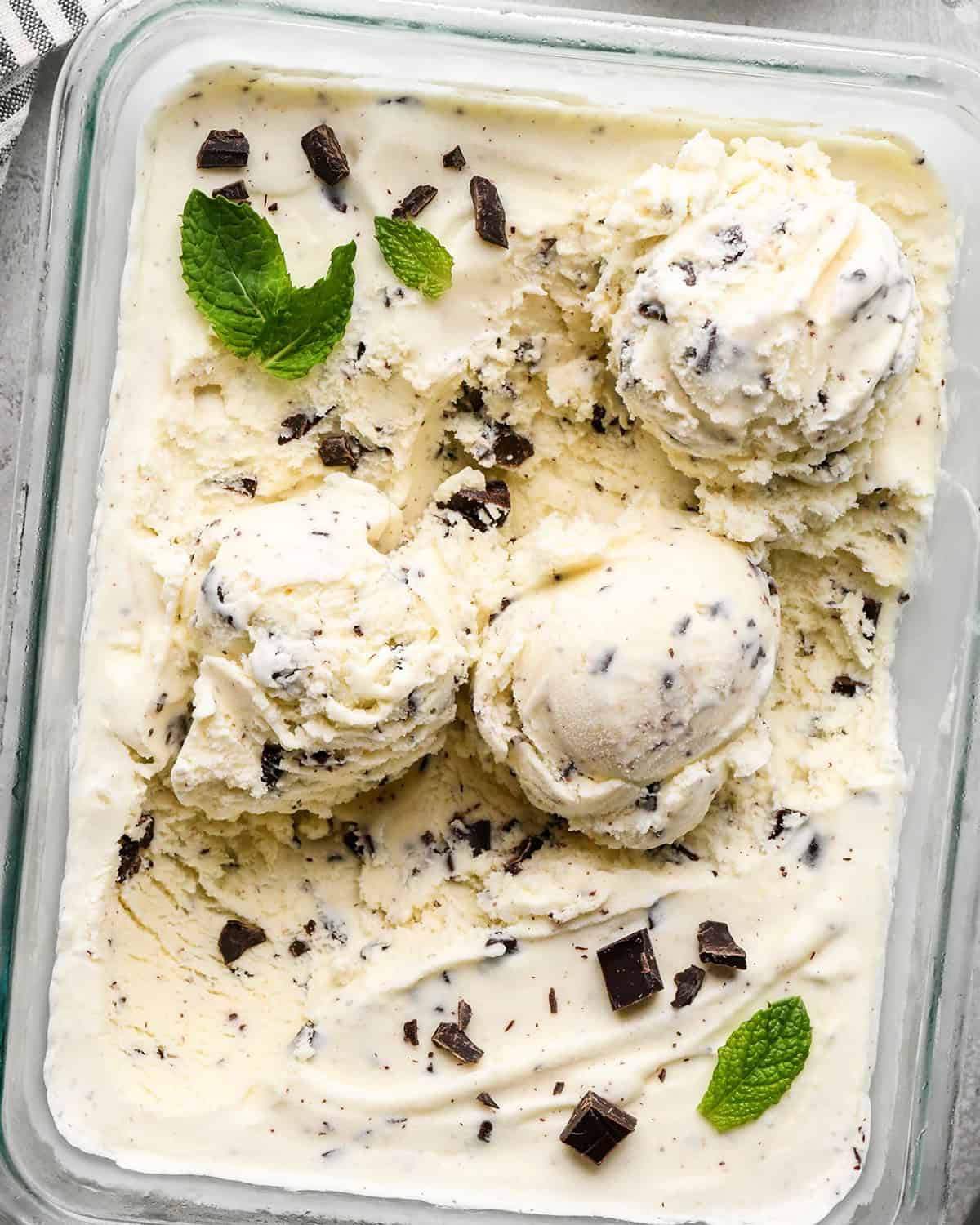 Mint Chocolate Chip Ice Cream in a glass container with 3 scoops scooped out of it