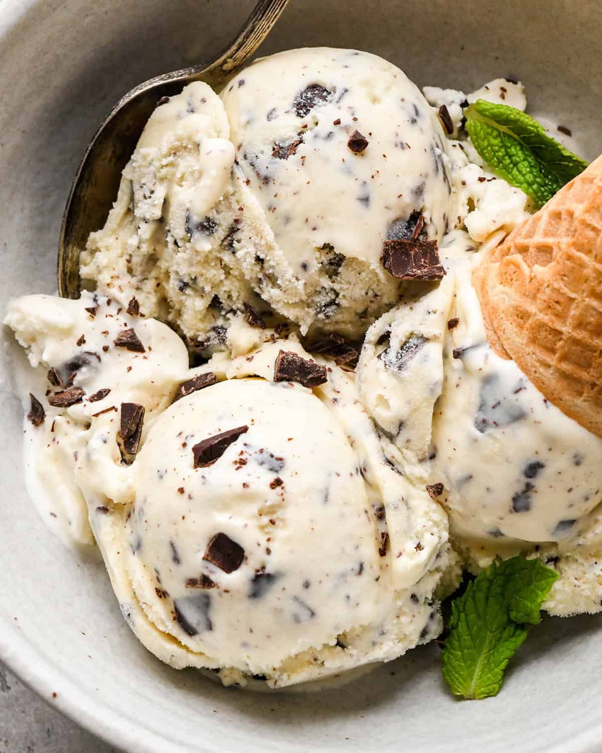 3 scoops of Mint Chocolate Chip Ice Cream in a bowl with a cone and fresh mint