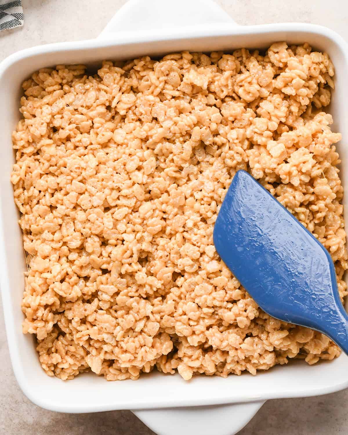 Peanut Butter Rice Crispy Treats mixture being pressed into a baking dish