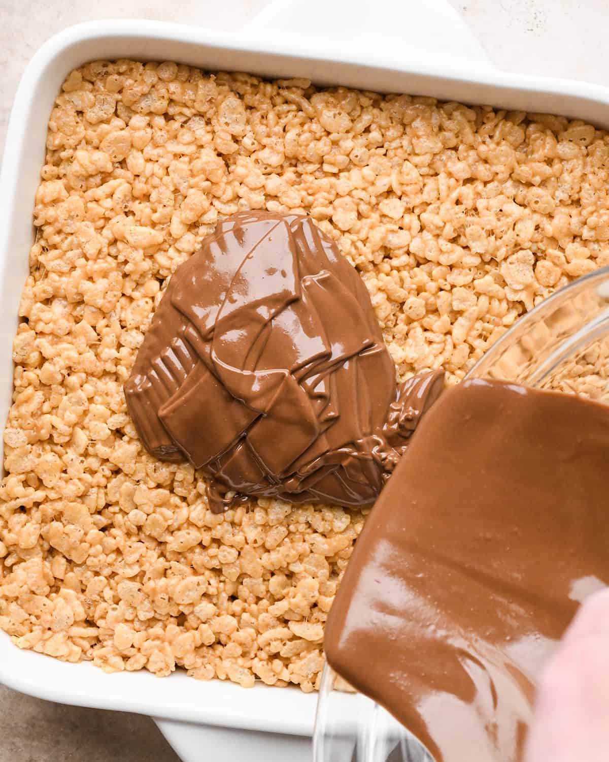 chocolate peanut butter mixture being poured onto Peanut Butter Rice Crispy Treats
