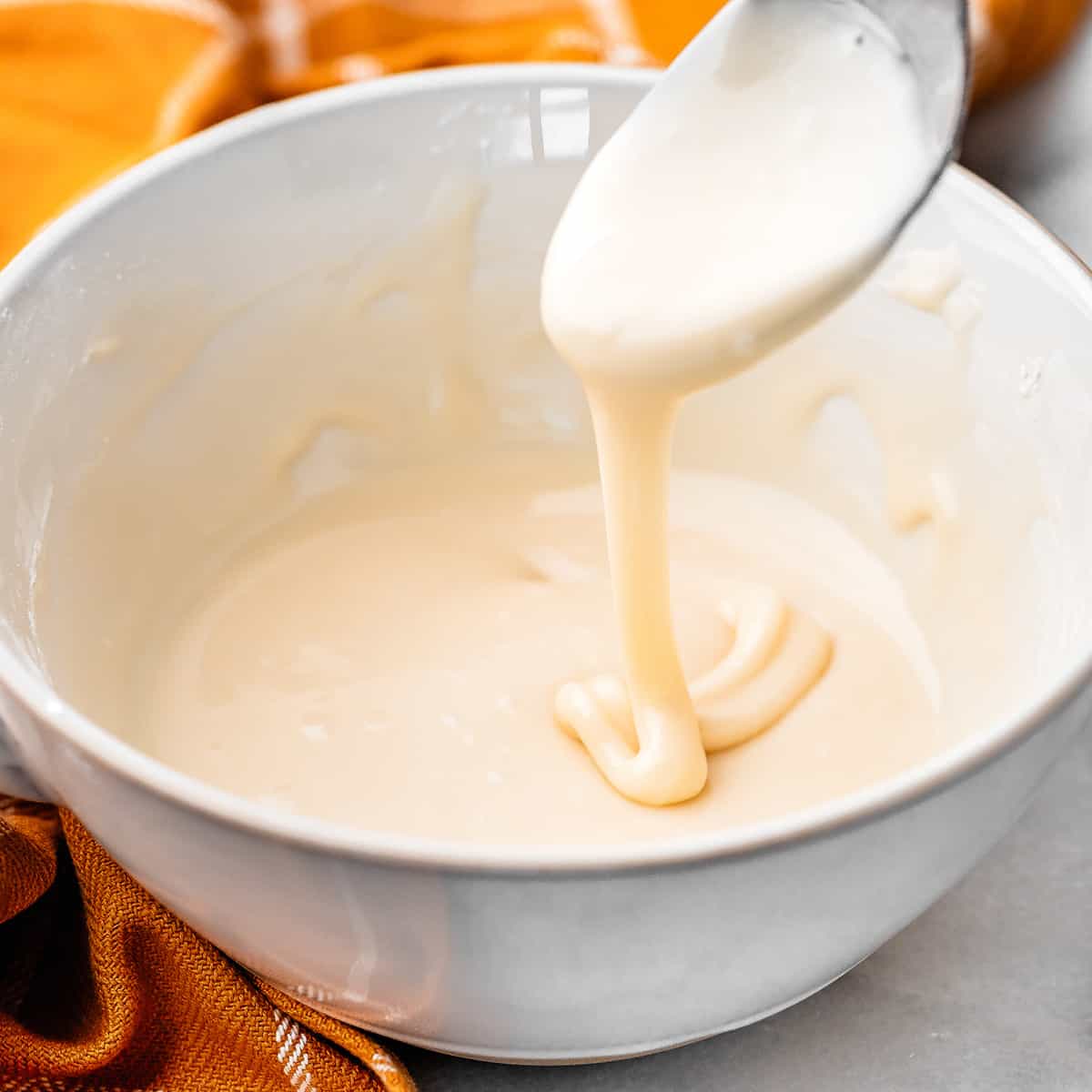 a spoon dripping maple glaze in a bowl of maple glaze