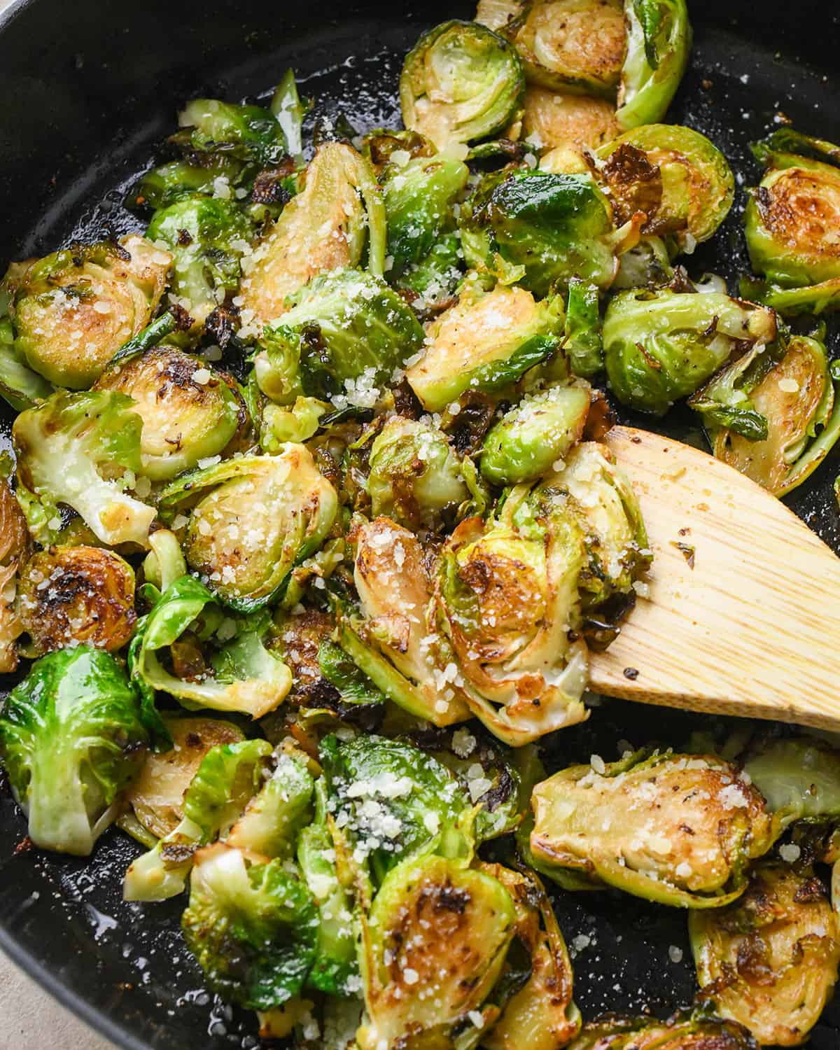 Sautéed Brussels Sprouts in a skillet with a wooden spatula