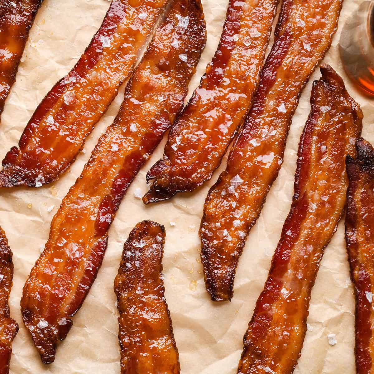 Crispy maple-glazed bacon strips topped with flaky sea salt on parchment paper.